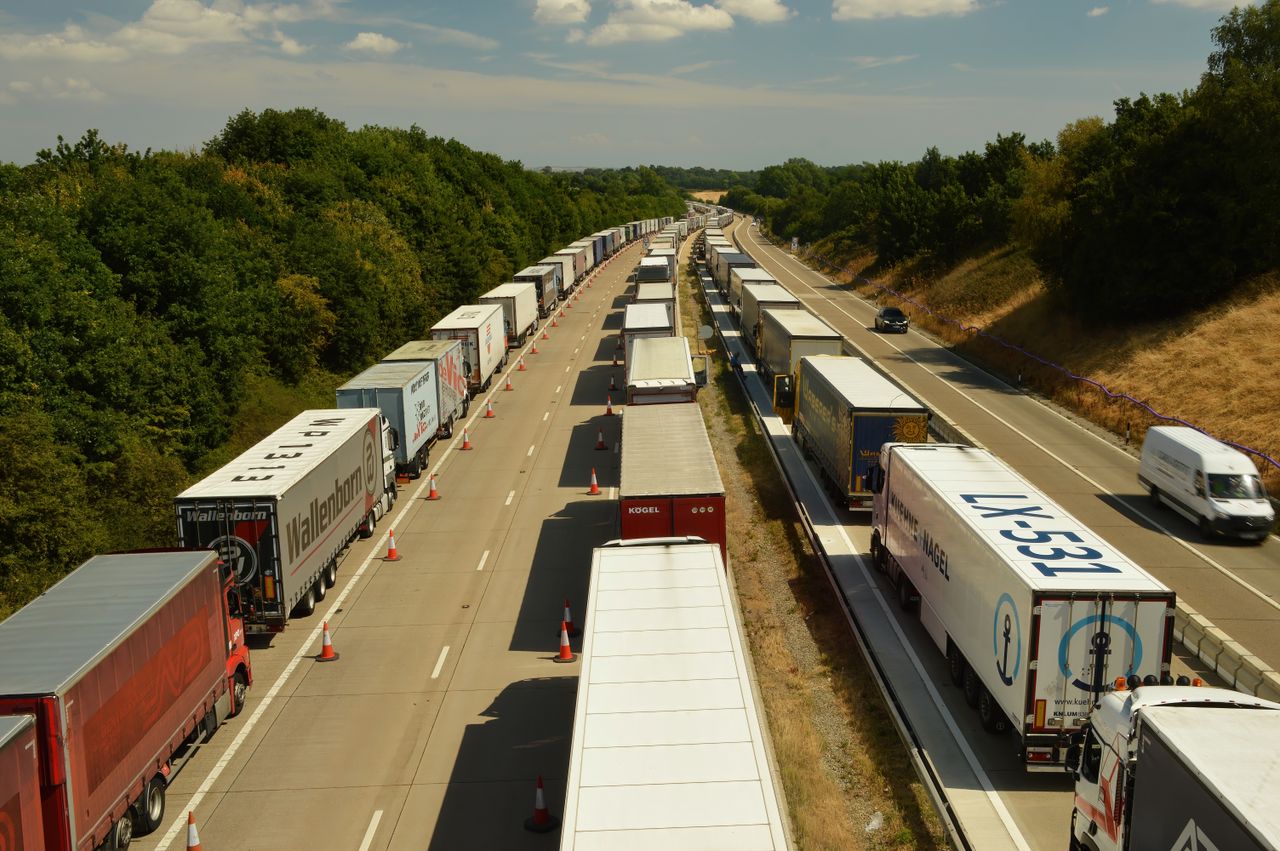A high-angle shot of trucks and trailers in traffic on a highway in England beneath a bright sky.