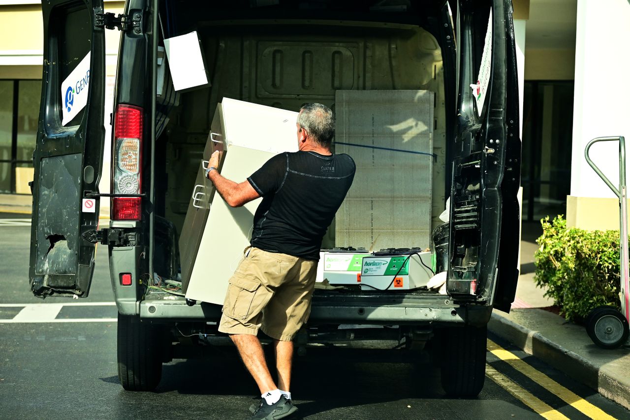 experience-img Adult man loading furniture into an open van in a parking lot, daytime setting.