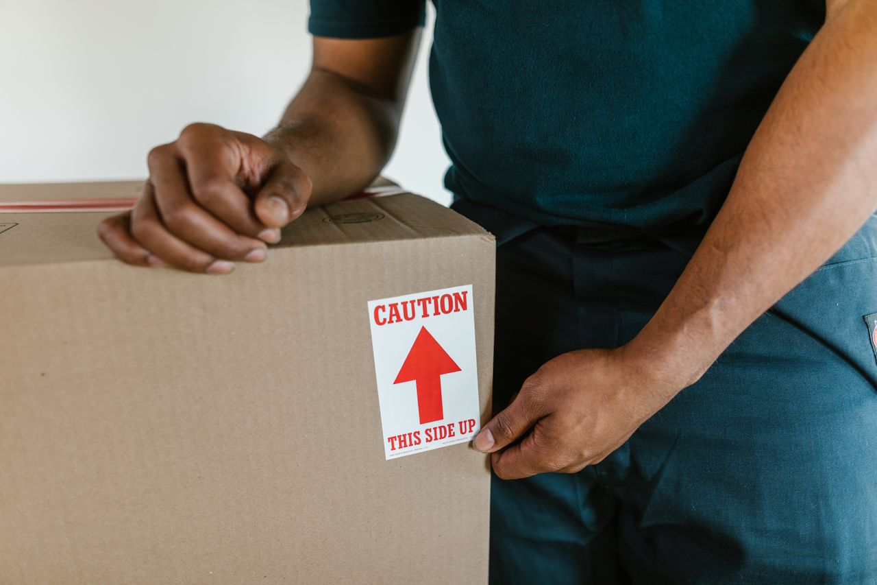 our-journey-01 A person handling a moving box with a 'caution this side up' label indoors.